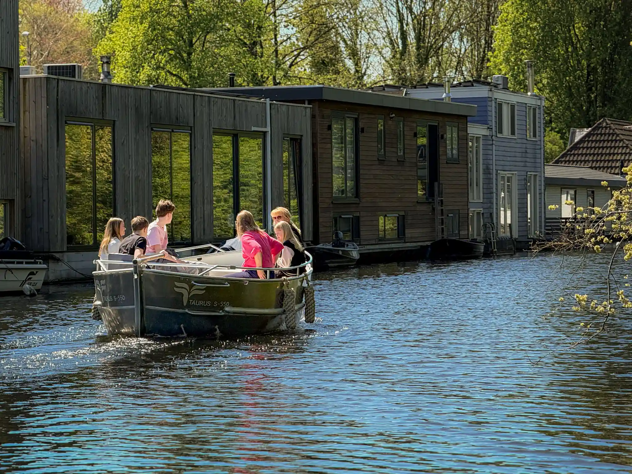 Groep mensen vaart in een elektrische sloep door de grachten van Rotterdam langs woonboten bij Delfshaven