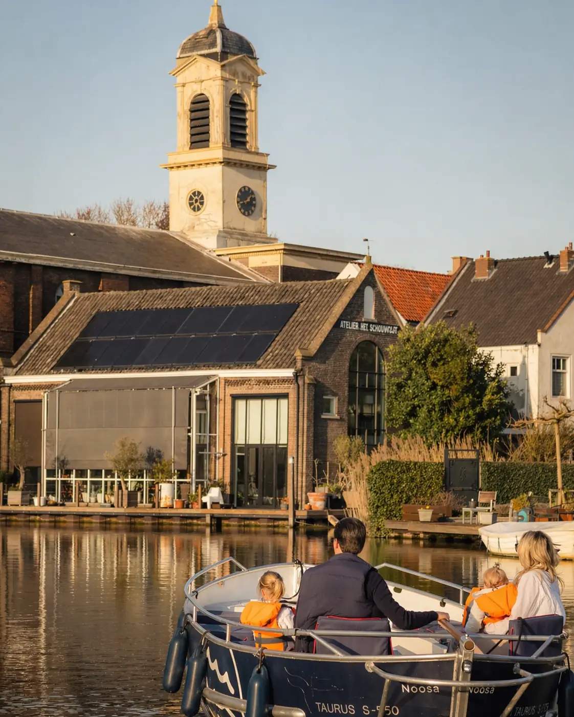 Gezin in sloep op rustige gracht met historische gebouwen en kerktoren in warm avondlicht